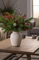 Decorative arrangement of greenery and red berries in a white vase on a wooden table.