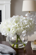 White flowers in a clear vase on a wooden surface with a blurred background