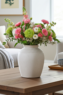 White vase with pink, green, and white flowers on a wooden table in a living room.