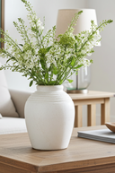 White vase with greenery on a wooden table in a living room setting
